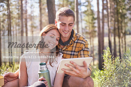 Young couple camping, drinking coffee and using digital tablet in sunny woods