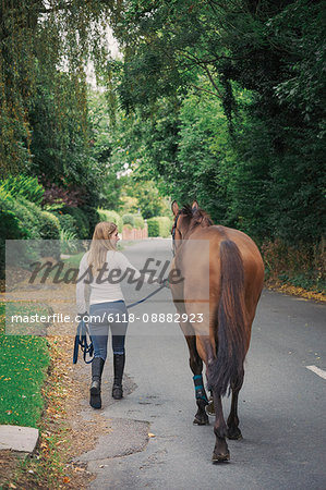 Rear view of woman and a brown horse walking along a road.