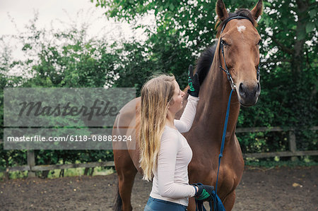 A young woman and a bay thoroughbred racehorse in a paddock