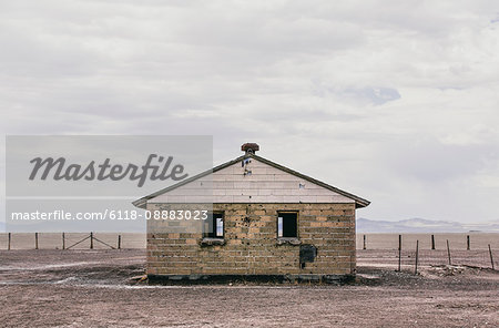 A derelict house in a flat landscape with mountains in the distance under a cloudy sky.