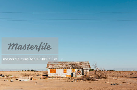 A boarded-up wooden house in an arid landscape against a blue sky.
