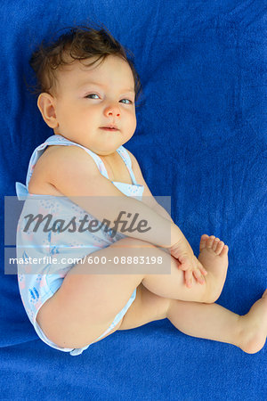 One year old baby girl wearing a swimsuit lying down on a blue beach towel