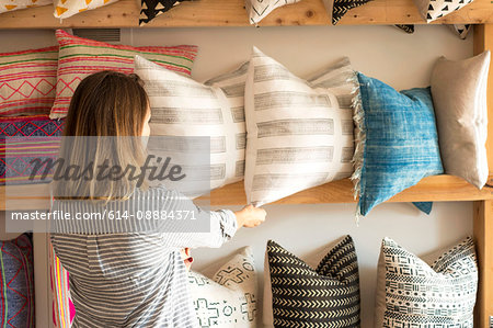 Rear view of female interior designer adjusting cushions on shelves in retail studio
