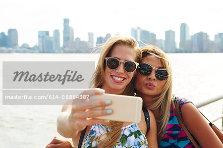 Two women taking smartphone selfie on waterfront with skyline, New York, USA