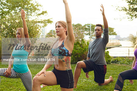 Men and women practicing yoga pose on one knee in park
