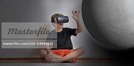 Young boy sitting cross legged, wearing virtual reality headset, reaching out to touch planet, digital composite