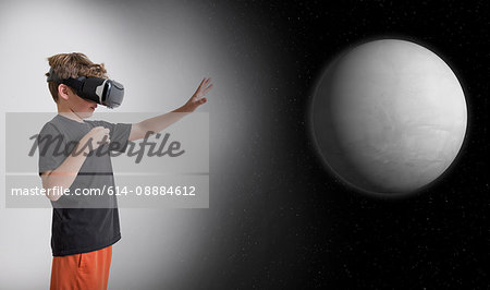 Young boy wearing virtual reality headset, reaching out to touch planet, digital composite
