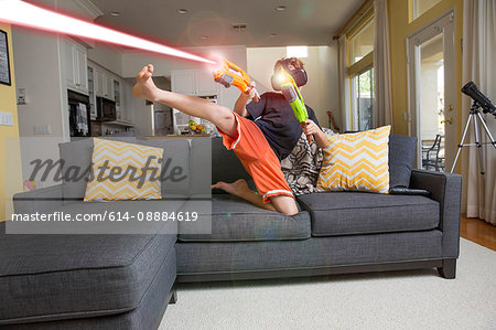 Young boy on sofa, wearing virtual reality headset, kicking leg, firing laser guns, digital composite