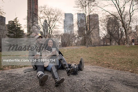 Couple sitting on rock in park with takeaway coffee