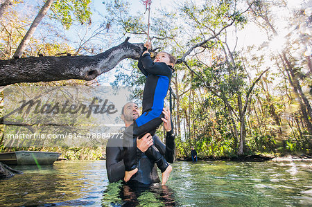 Father in river helping daughter with rope swing on tree, Chassahowitzka, Florida, USA