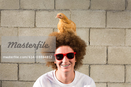 Portrait of teenage boy with red afro hair, chicken sitting on head