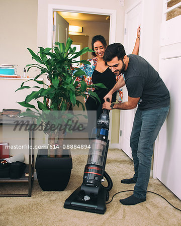 Woman supervising man vacuuming carpet