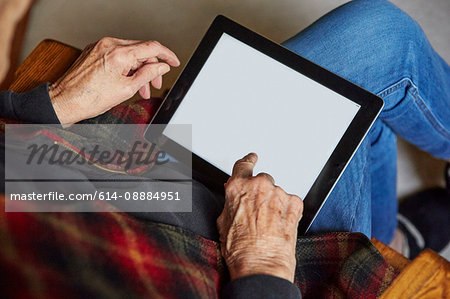 Senior woman sitting in chair, using digital tablet, elevated view