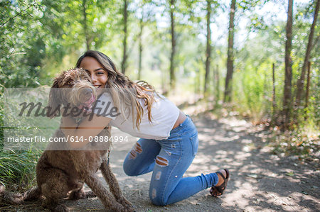 Portrait of teenage girl hugging cute dog on woodland path