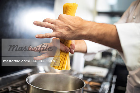 Chef putting spaghetti in saucepan on stove, close-up, overhead view