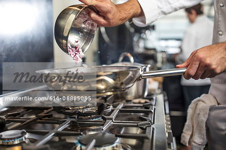 Chef pouring sliced red onions into pan on stove, close-up