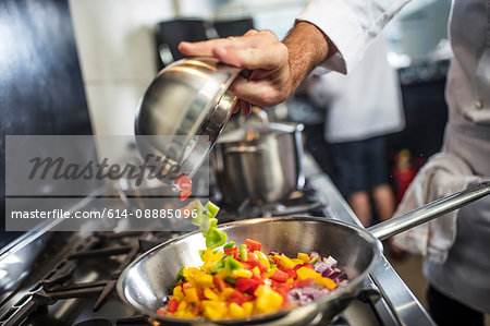 Chef pouring sliced vegetables into pan on stove, close-up