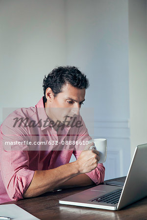 Man drinking coffee while using laptop computer