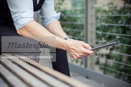 Man sitting on bench, using digital tablet, cropped