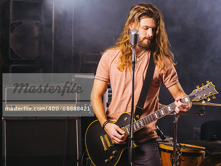 Photo of a young man with long hair and beard playing electric guitar on stage.