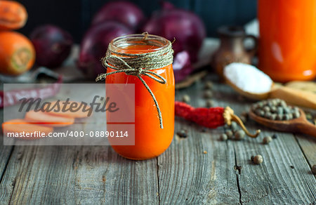 Fresh carrot juice in a glass jar among the spices and fresh vegetables