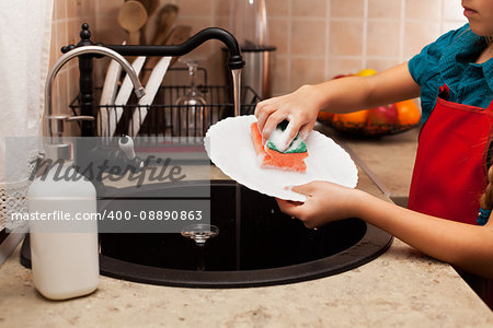 Child washing a plate with sponge at the kitchen sink - closeup, shallow depth