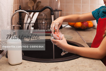 Washing the dishes - child hands cleaning a glass with sponge and foamy detergent at the kitchen sink, shallow depth
