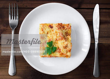 Close-up of a traditional lasagna topped with parskey leafs served on a white plate on dark wooden table. vertical