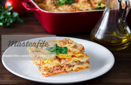 Close-up of a traditional lasagna topped with parskey leafs served on a white plate on dark wooden table