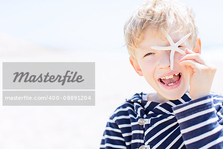 cheerful smlling positive boy winking and holding starfish in the hand being playful and enjoying nice weather at the beach, summer vacation concept, copyspace on the left