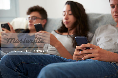 Three teenagers sitting together using smartphones at home