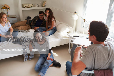 Teenage friends hanging out in bedroom, over shoulder view