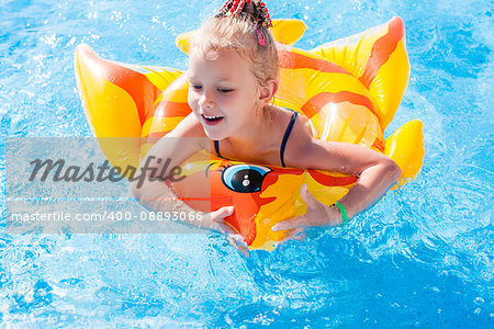 Portrait of cute happy little girl having fun in swimming pool, floating in blue refreshing water with inflatable ring, active summer vacation on the beach.