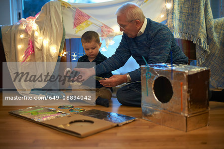 Boy and grandfather sitting on floor making robot costume