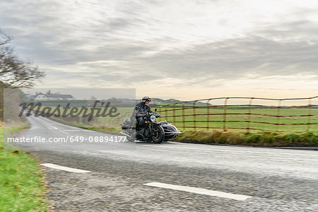 Senior man and grandson riding motorcycle and sidecar on rural road