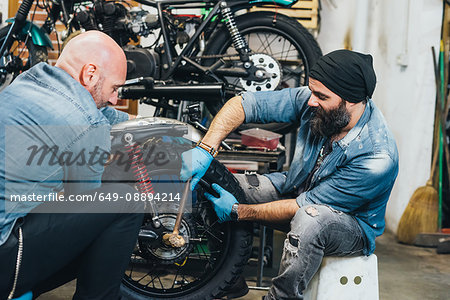 Two mature men, working on motorcycle in garage