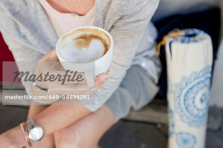 Mid section of woman with empty coffee cup at city sidewalk cafe