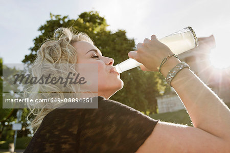 Mid adult woman in sunlit park drinking lemonade