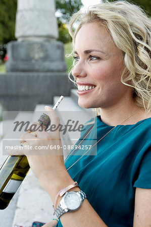 Mid adult woman sitting on park stairs drinking beer