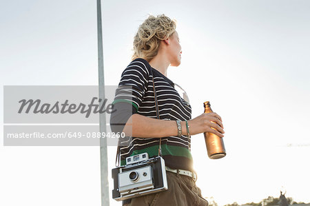 Mid adult woman carrying beer bottle and vintage camera in park