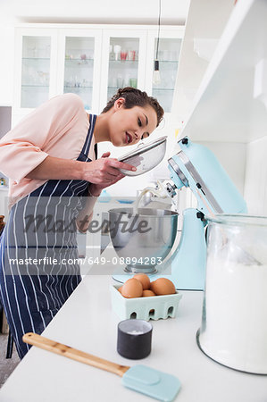 Young woman sifting flour into food mixer bowl at kitchen counter