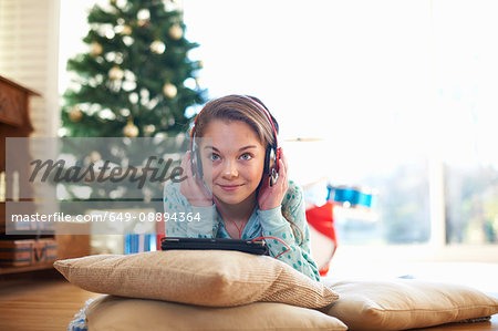 Girl lying on living room floor listening to headphones at Christmas