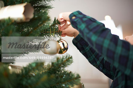 Hands of boy placing baubles on christmas tree