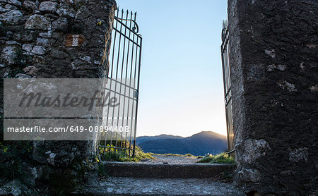 Stone walls and old open gates with distant view of mountains at sunset