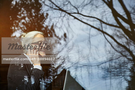 Home window view of senior businesswoman making smartphone call