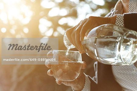 Hands of senior woman pouring glass of water by window