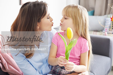 Girl handing tulip to mother and puckering lips on sofa