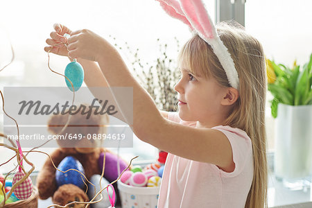 Girl in bunny ears making easter egg decoration in living room