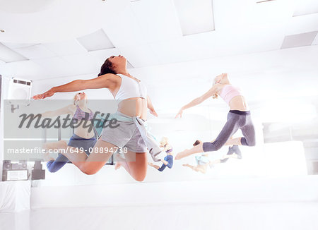 Young female ballet dancers practicing in dance studio, jumping in unison