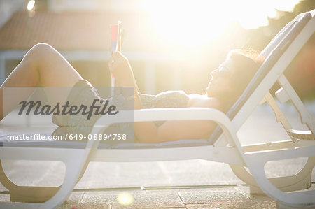 Mature woman reclining in sunlit lounger reading magazine, Sintra, Portugal